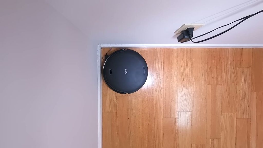 Eufy C10 städar längs väggen på ett trägolv, sedd ovanifrån